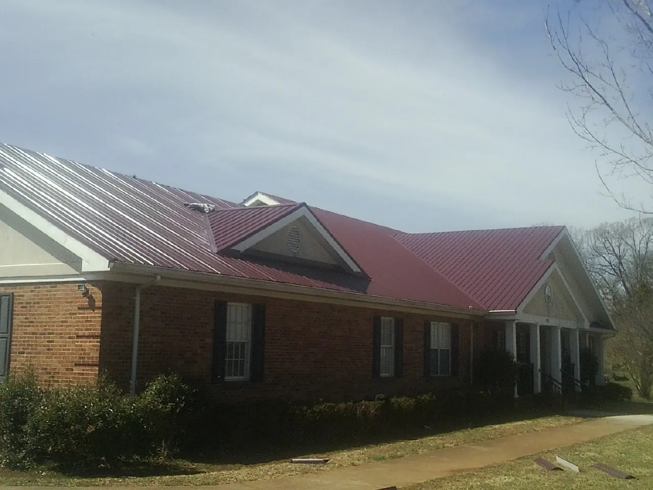 Red metal roof with gabled entries on a long brick building, from a Hail Damage Roof Repair job in Kahului