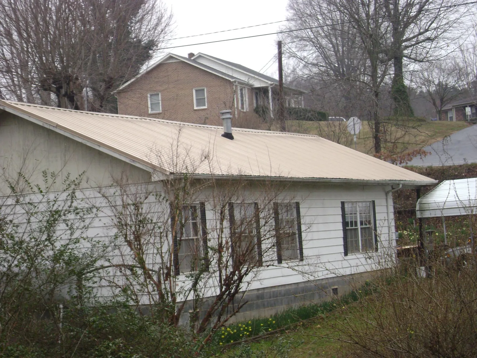 Tan metal roof on a white sided house set into a hillside — Commercial Roofing by Roofing Brothers in Kahului